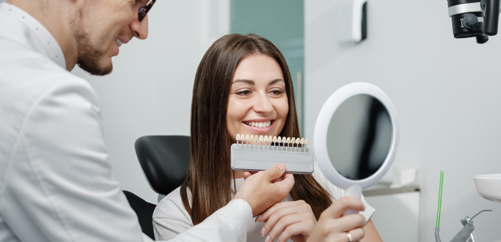 dentist holding tooth-shade matching tool against woman's smile