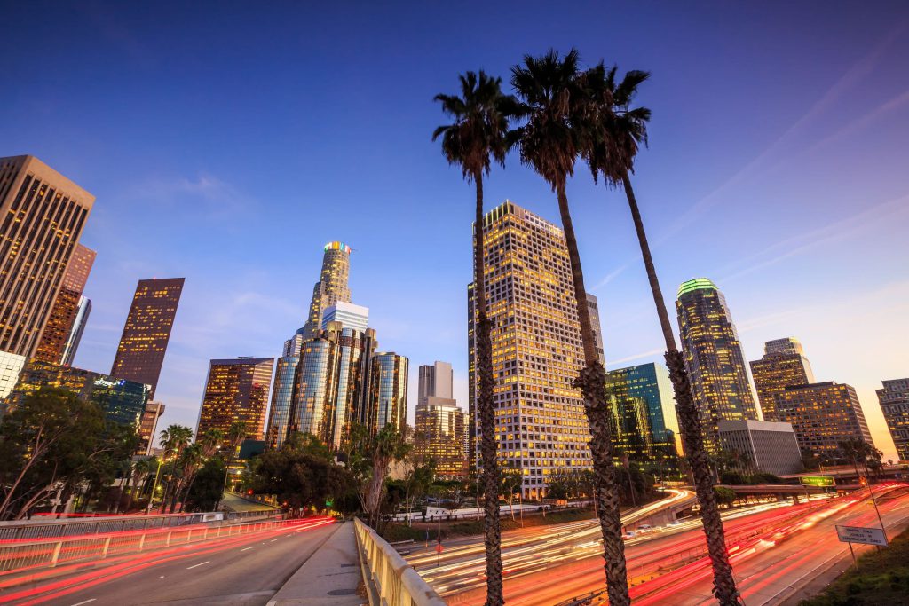 Downtown Los Angeles skyline at dusk seen past a row of palm trees