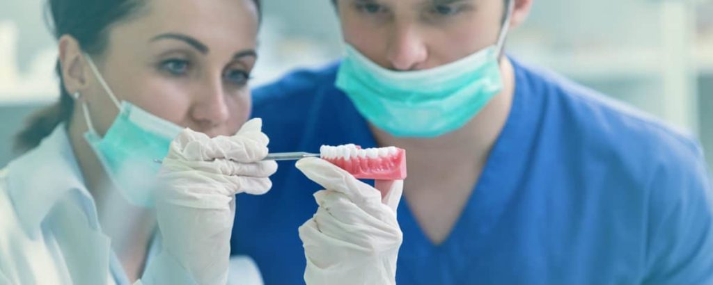 Two masked dental technicians setting teeth into a denture