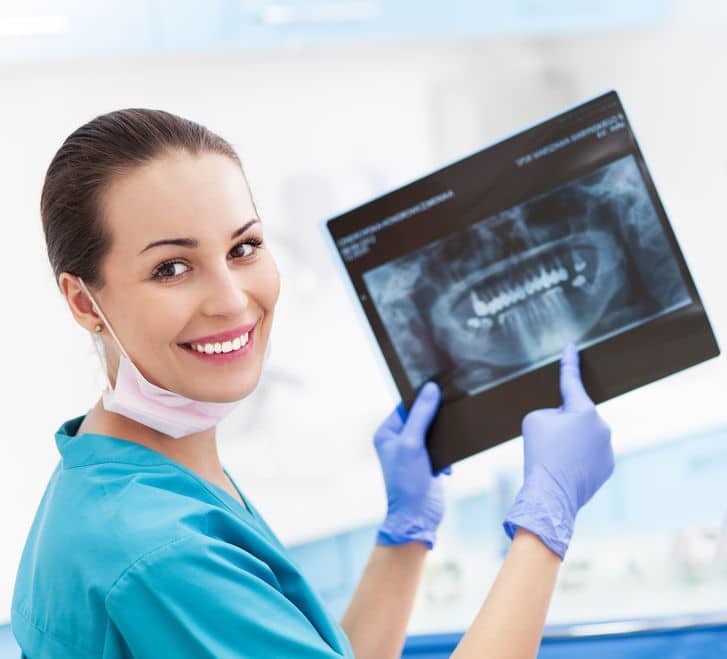 Dentist in scrubs holding up a dental X-ray and pointing at it