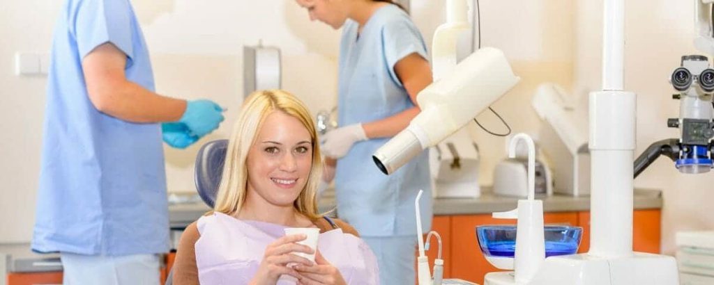 Patient seated in the chair while two clinicians position dental imaging equipment