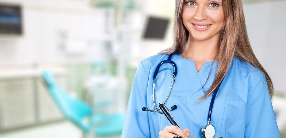 Smiling clinician in blue scrubs standing in a treatment room