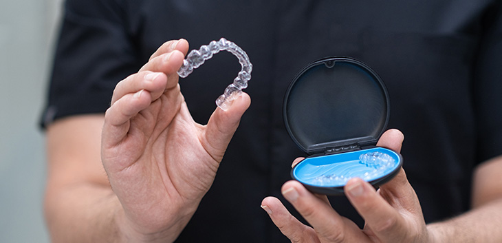 Hands holding a clear aligner and its case