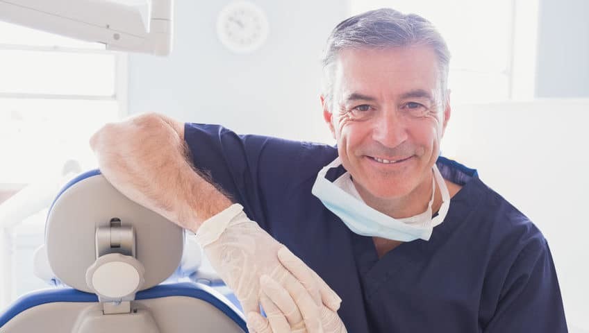 Smiling dentist standing beside a dental chair
