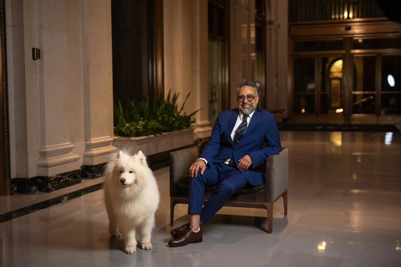 Dr. Kourosh Yousefzadeh in a navy suit, seated in the lobby at 523 West Sixth Street with the practice dog beside him