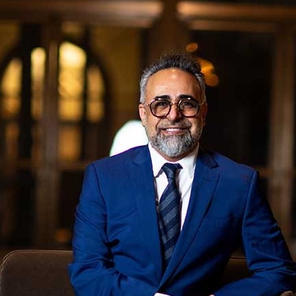 Dr. Kourosh Yousefzadeh in a navy suit and striped tie, seated in the practice lobby