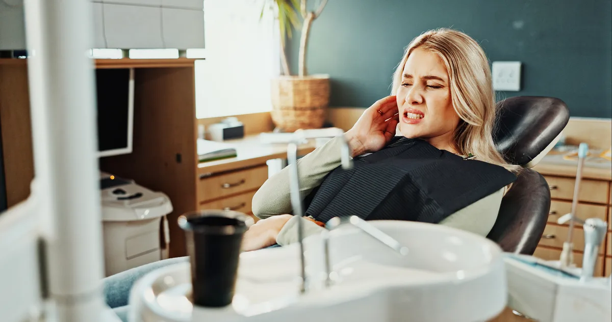 A woman in a dental chair holding her jaw in discomfort