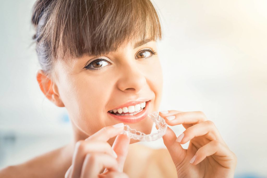 Smiling woman holding a clear aligner tray