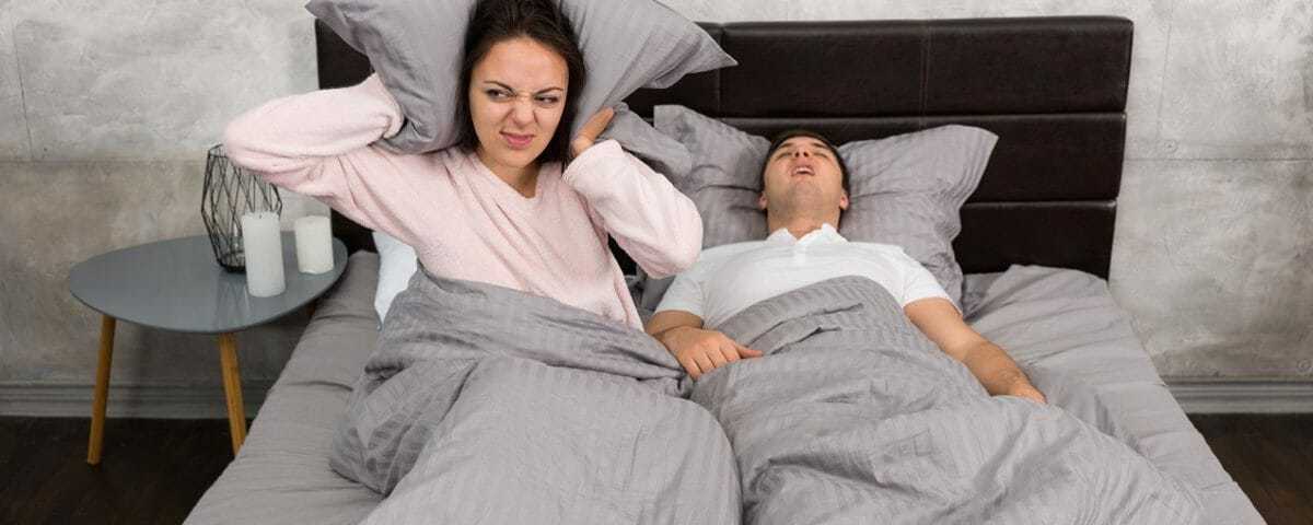 Woman covering her ears in bed beside a snoring partner