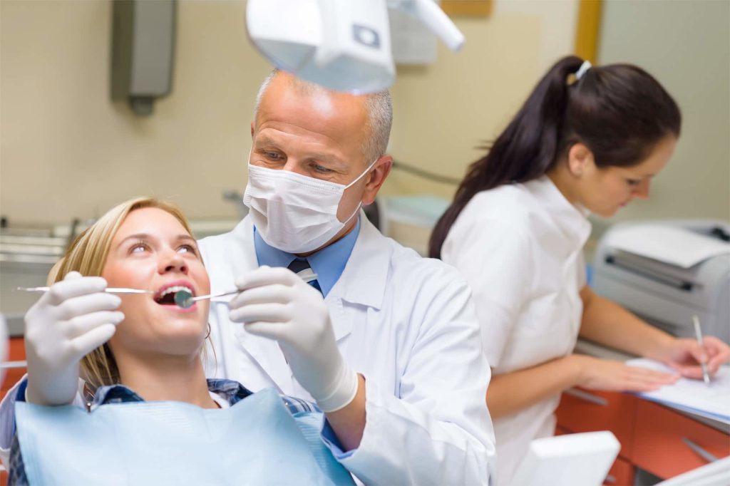 Dentist and assistant treating a patient while a colleague works at a desk behind them