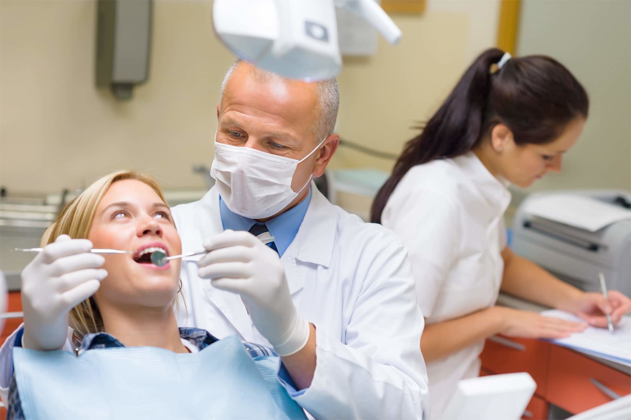 Dentist and assistant treating a patient while a colleague works at a desk behind them