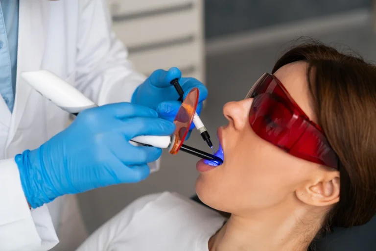 A dentist treating a patient wearing protective glasses with a handheld dental light