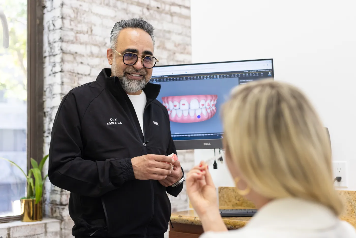 Dr. Kourosh Yousefzadeh showing a patient a digital smile design on the wall screen