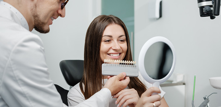 Dentist holding a tooth shade matching tool against a woman's smile
